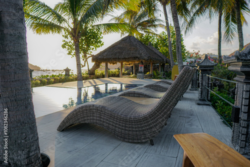 Sunchairs at the swimming pool.Relaxing in swimming pool at spa resort.Beach chairs under coconut palm near the sea vacation concept photo