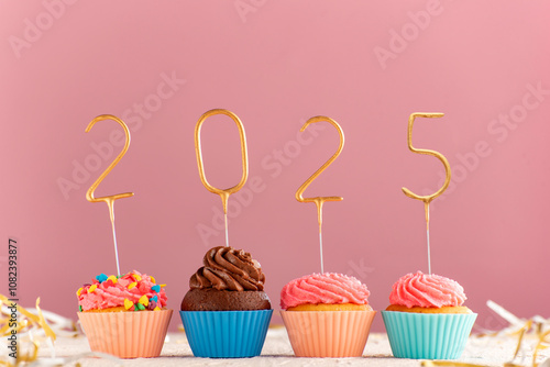 Cupcakes or muffins with buttercream frosting decorated with gold 2025 numbers on pink background.