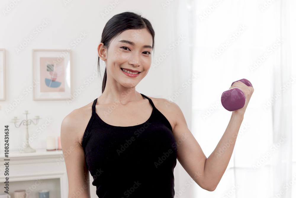 Asian beautiful woman doing exercise with dumbbell at home. Happy smiling young athletic female lifting dumbbell for training her body. Sporty girl practices work out. Healthy sport hobby lifestyle. Asian beautiful woman doing exercise with dumbbell at home. Happy smiling young athletic female lifting dumbbell for training her body. Sporty girl practices work out. Healthy sport hobby lifestyle.