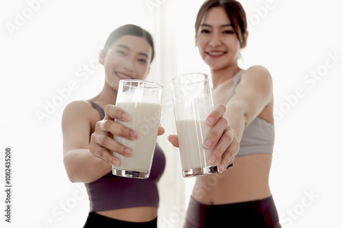 Two glasses of milk in hand of sporty girl buddy. Happy beautiful Asian women hold milk glass for drinking after workout exercise. Food rich in vitamins and calcium. Healthy food and sport lifestyle