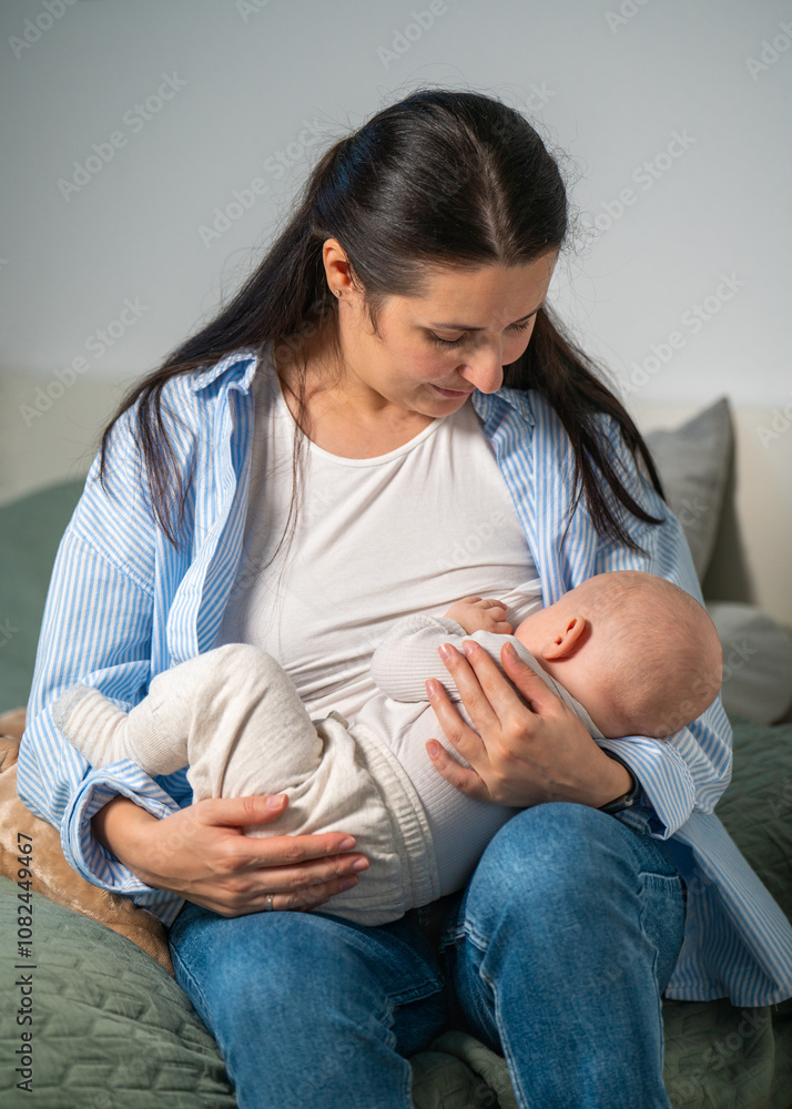 Fototapeta premium Mother breastfeeds her cute newborn baby sitting on her bed at home. Milk from mother breast is a natural food and medicine for babies.