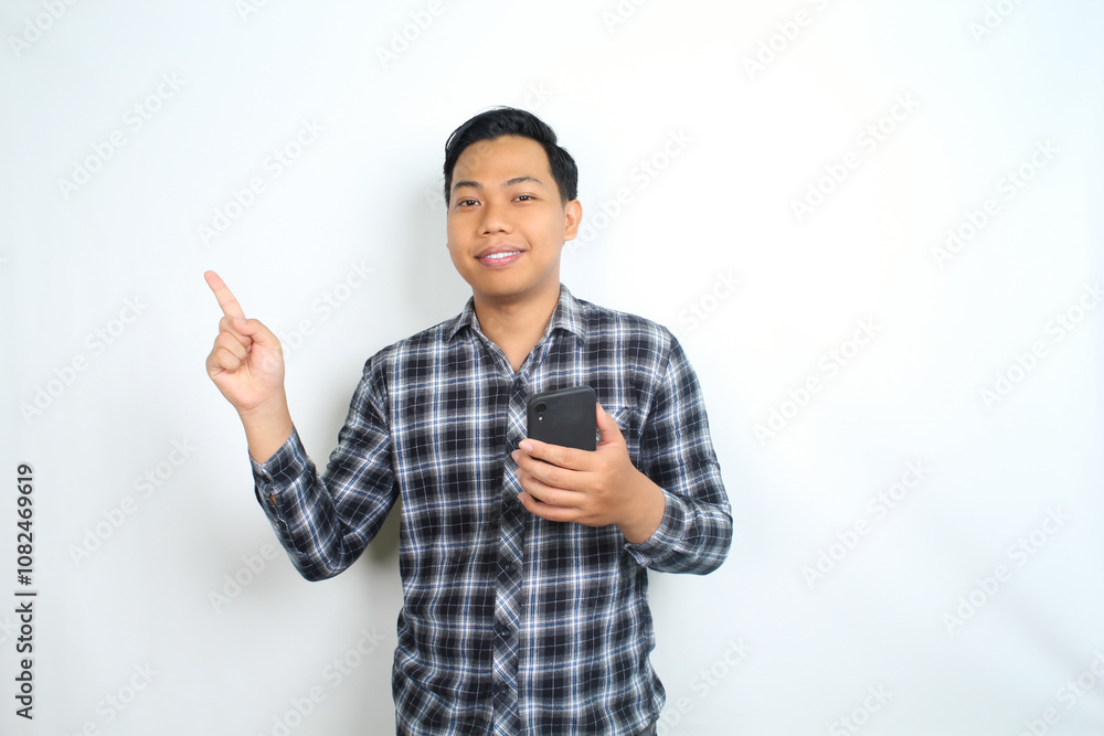 smiling asian man pointing to copy space with holding mobile phone isolated on white background smiling asian man pointing to copy space with holding mobile phone isolated on white background