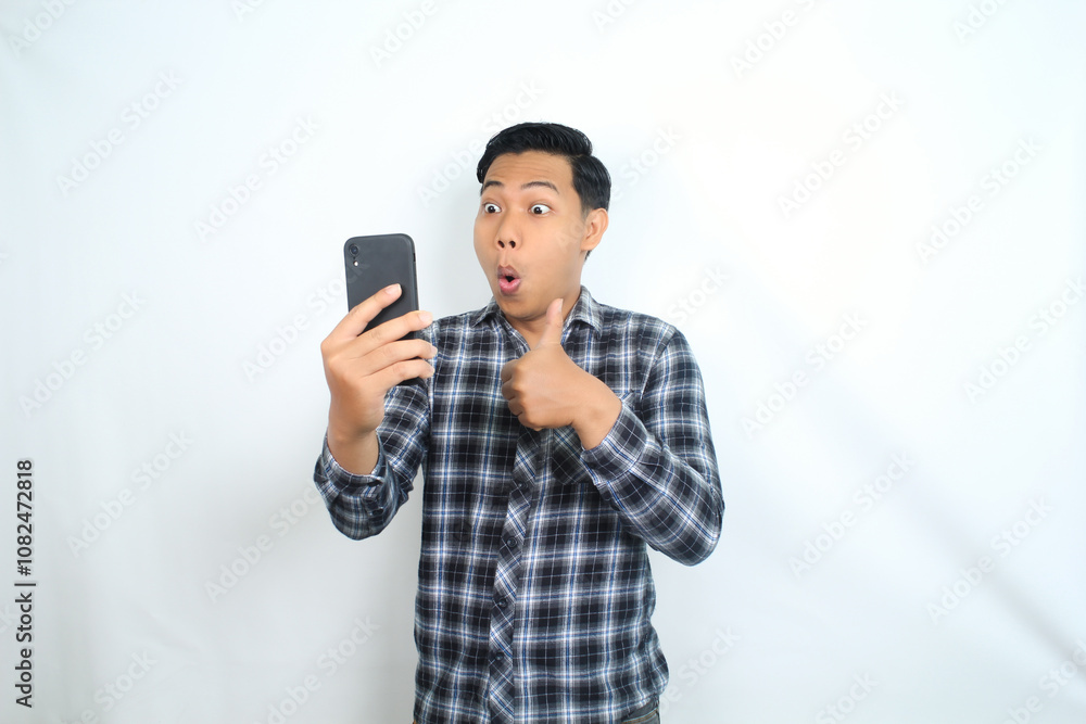 asian man give thumb up with shocked funny face and holding mobile phone isolated on white asian man give thumb up with shocked funny face and holding mobile phone isolated on white
