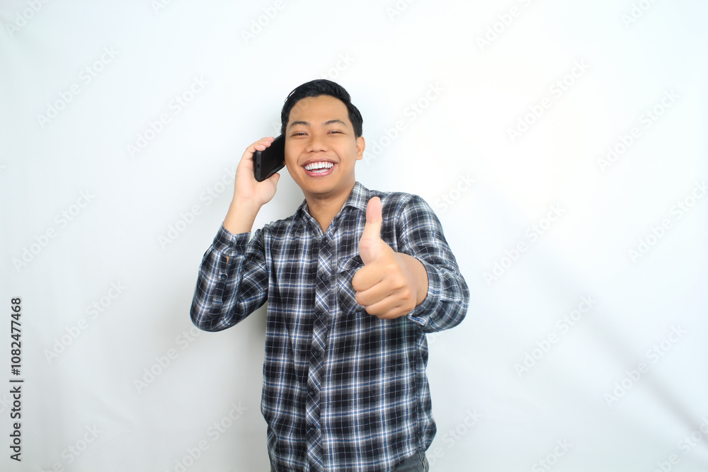 happy asian man showing thumb up while talking on mobile phone wearing plaid shirt isolated on white happy asian man showing thumb up while talking on mobile phone wearing plaid shirt isolated on white