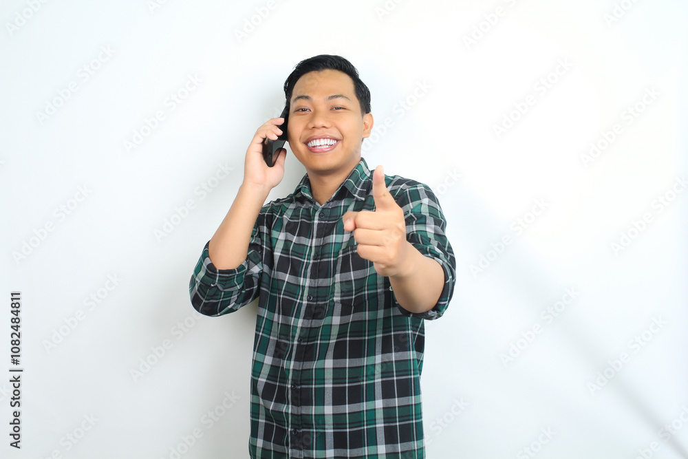 cheerful and carefree asian man wearing casual clothes pointing his hand while talking on cellphone, calling, with smiling face isolated on white background cheerful and carefree asian man wearing casual clothes pointing his hand while talking on cellphone, calling, with smiling face isolated on white background
