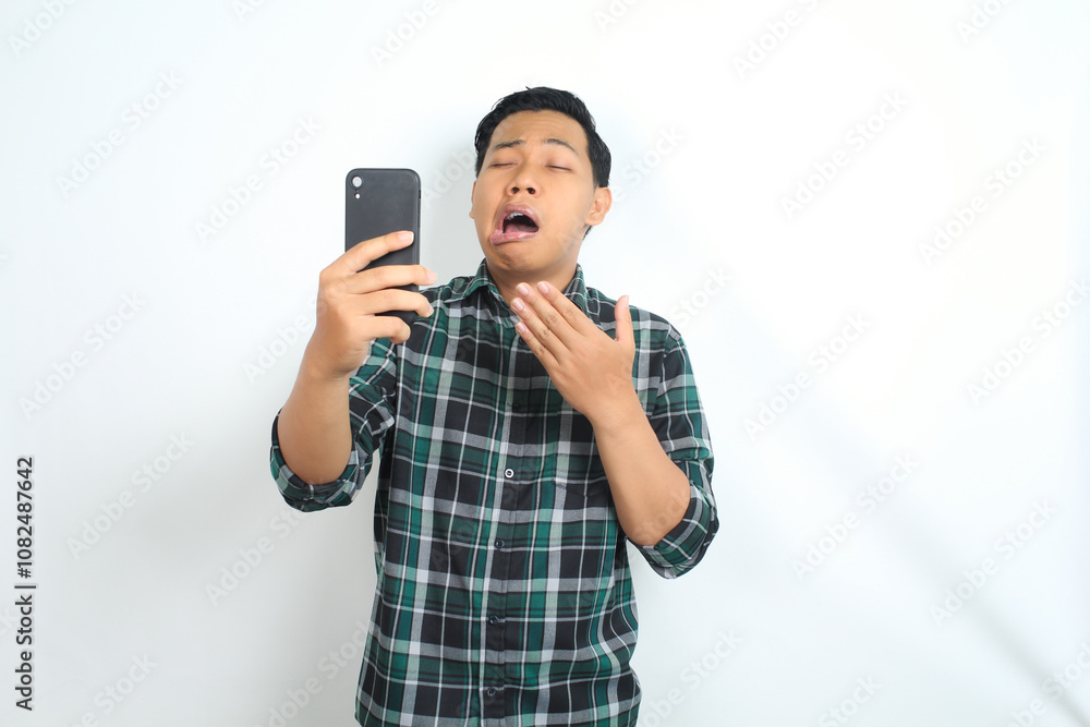 asian man yawning while holding smartphone, covering mouth, isolated on white background asian man yawning while holding smartphone, covering mouth, isolated on white background