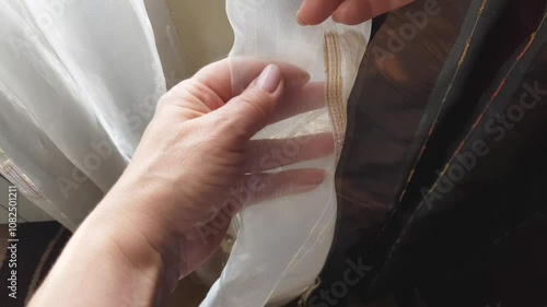 Close-up of a woman's hand touching and moving the fabric of the curtains in her room, viewing the quality of the seams on the curtains, 4k video photo