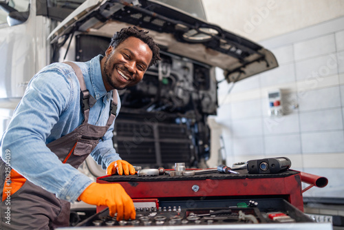 Truck service and maintenance. Portrait of smiling truck mechanic standing by toolbox inside workshop.