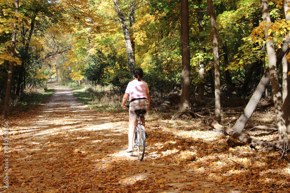 Woman riding a bicycle on the Des Plaines River Trail in autumn at Camp Ground Road Woods in Des Plaines, Illinois Woman riding a bicycle on the Des Plaines River Trail in autumn at Camp Ground Road Woods in Des Plaines, Illinois
