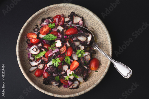 Salad with octopus stewed in wine, tomatoes, onions and aromatic herbs, Mediterranean cuisine. What to cook from octopus  on the second day. Black background photo