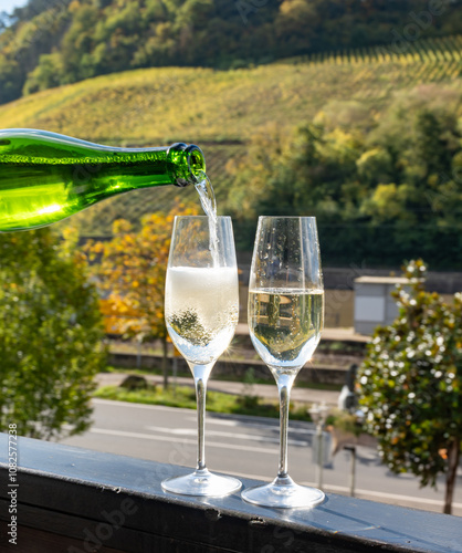 Tasting sparkling white wine, traditional champagne method making of cremant in caves on Moselle river valley in Luxembourg, glasses of wine and view on terraced vineyards photo