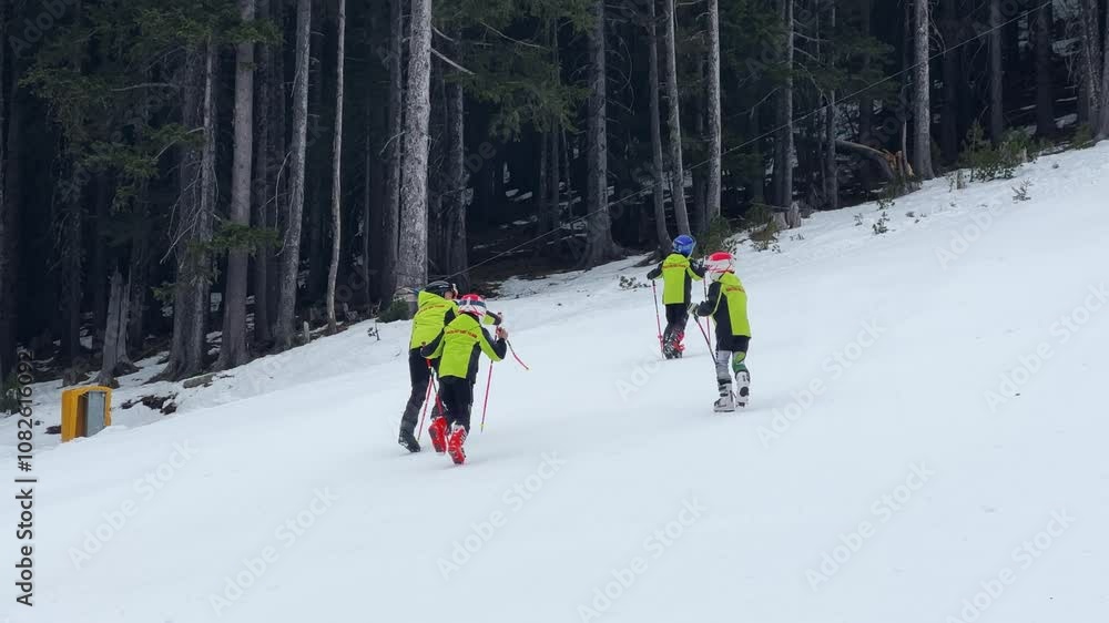 Young skiers in bright jackets training on a snow-covered mountain slope. A group of children learn skiing techniques