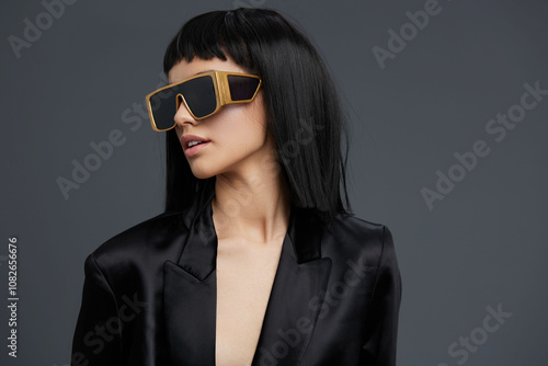Wallpaper Mural Woman with black hair, sunglasses, and a black blazer standing against a gray background with a gold frame on her head, exuding a stylish and contemporary fashion statement Torontodigital.ca