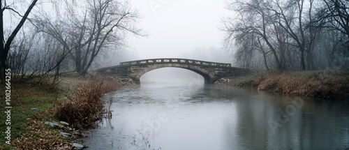 A foggy bridge arches gracefully over a tranquil river, framed by leafless trees, exuding a sense of mystery and timelessness in the misty dawn.