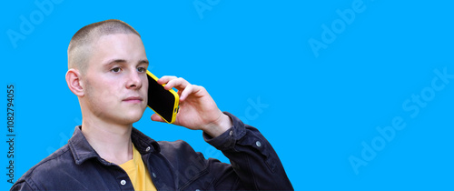 Young man talking on the phone outdoors in a casual setting with a bright blue background on a sunny day