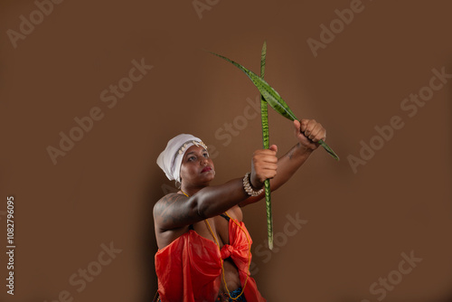 Woman in traditional Candomble clothing, holding the Espada de Sao Jorge plant and posing for a photo.