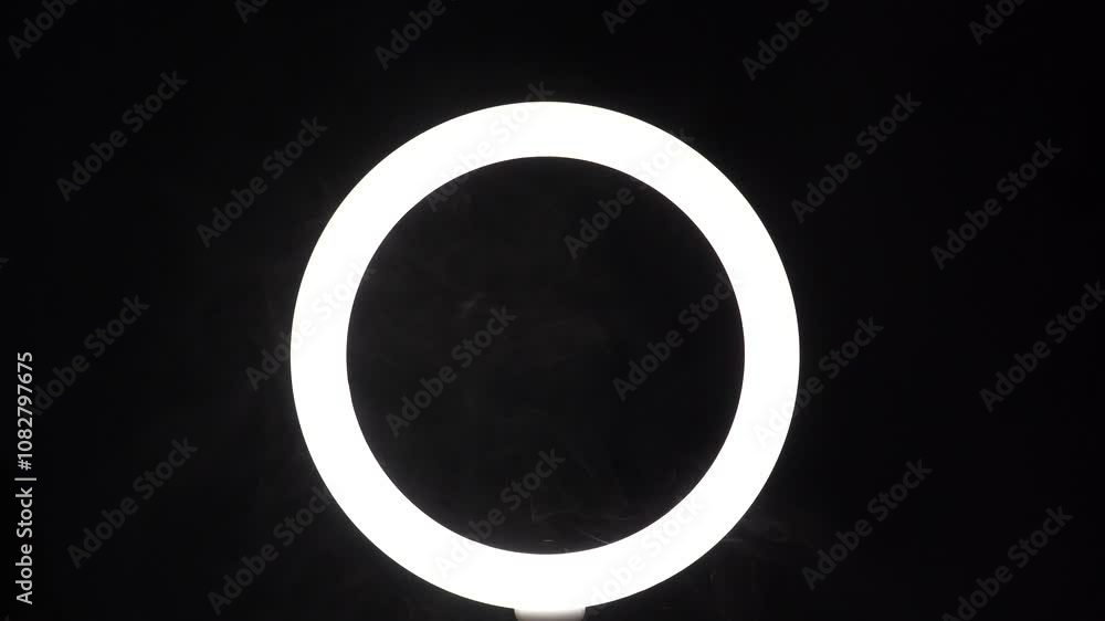 A stream of smoke in front of a ring of light from a led lamp on a black background close-up. The vaper blows steam in the frame. The concept of a dance club and a stage with spotlights A stream of smoke in front of a ring of light from a led lamp on a black background close-up. The vaper blows steam in the frame. The concept of a dance club and a stage with spotlights