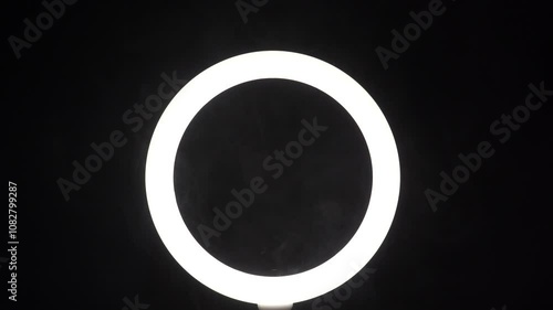 A stream of smoke in front of a ring of light from a led lamp on a black background close-up. The vaper blows steam in the frame. The concept of a dance club and a stage with spotlights