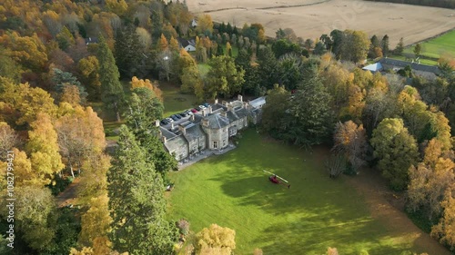 helicopter parked grass luxurious country house estate autumn trees forest background enhance richness property aerial drone panning shot hotel mansion view 