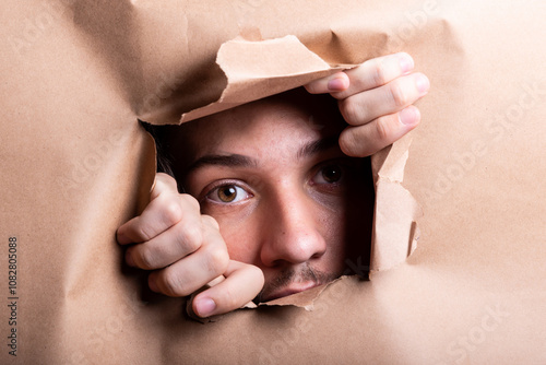 Man eye looking through a hole in a sheet of paper.