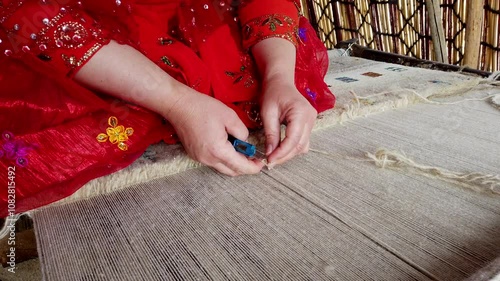 Craftswoman in a red dress ties knots on a traditional loom, showcasing the intricate art of carpet weaving