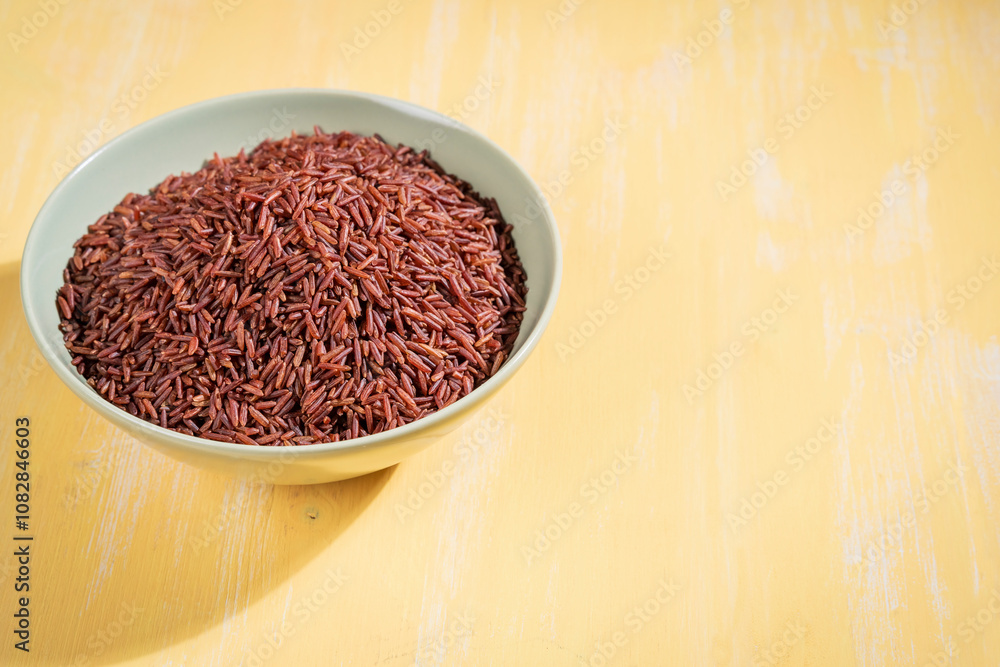 A bowl of red rice is placed on a yellow table.The raw rice is spread out in the bowl, copy-space. A bowl of red rice is placed on a yellow table.The raw rice is spread out in the bowl, copy-space.