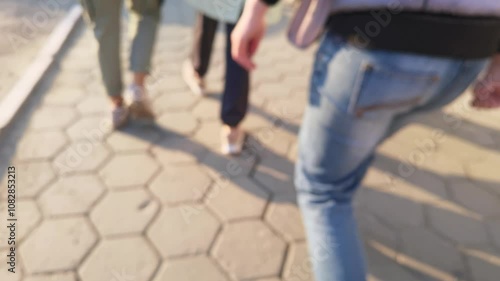 People walking on sunlit sidewalks in casual jeans during daytime commute.