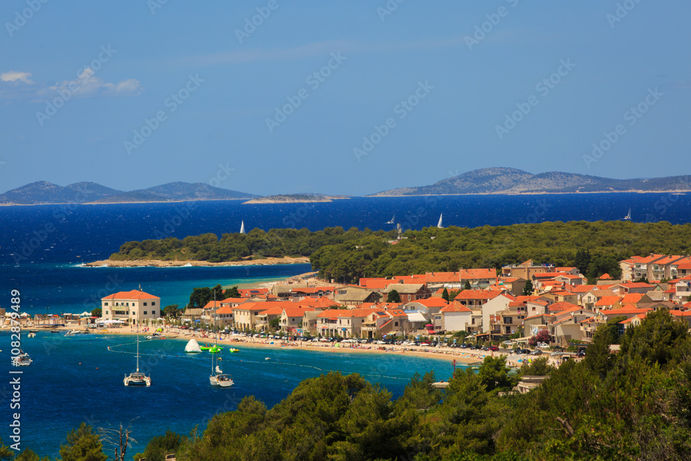 Fototapeta premium A distant view of the charming city of Primosten, Croatia, with clear blue skies and turquoise waters creating a serene coastal scene