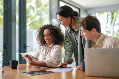 Canvas Print A mixed ethnicity group of young professionals collaborate with enthusiasm, using a tablet and a laptop in a sleek office environment, exemplifying teamwork and technological integration