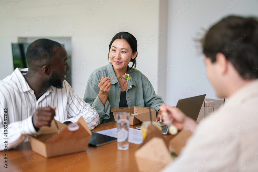 A group of young adult business professionals of diverse ethnic backgrounds enjoys a casual meal together, exchanging ideas in a sleek office environment. A group of young adult business professionals of diverse ethnic backgrounds enjoys a casual meal together, exchanging ideas in a sleek office environment.