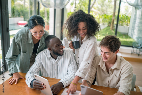 Fotografia Four young adult executives of varied ethnic backgrounds collaborate using a tablet and laptops in a well-lit modern office space, dressed in casual professional attire