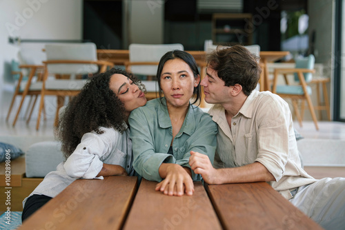 A group of young adult friends of diverse ethnicities relax together at home, displaying warmth and camaraderie as they lean in close around a wooden table.