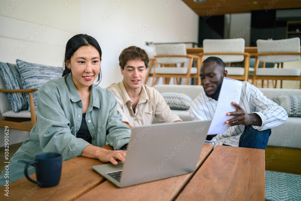 Three young adults of varied ethnicities engage in a collaborative work session in a cozy office lounge area, using a laptop and discussing documents. Three young adults of varied ethnicities engage in a collaborative work session in a cozy office lounge area, using a laptop and discussing documents.