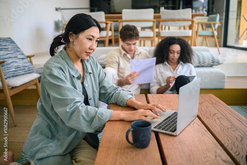 A diverse group of young professionals is engrossed in their work, utilizing a laptop and other tools while seated in a well-lit, contemporary office lounge.