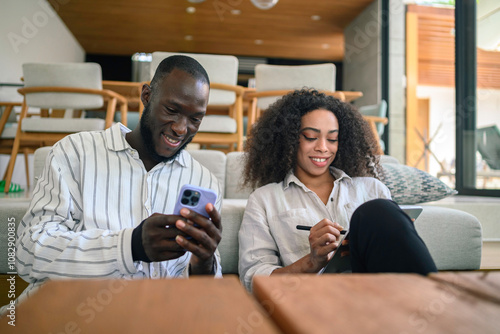 An African American woman and a Black man engage in productive teamwork at a modern workspace, utilizing a smartphone to enhance their discussion.