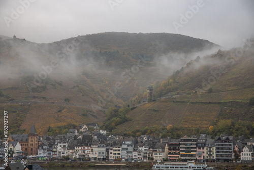 Landscape shot in autumn. a town meanders between a river and autumnal vineyards in the mist. A castle stands on the hill. Zell Mosel, Hunsrück, Rhineland Palatinate photo