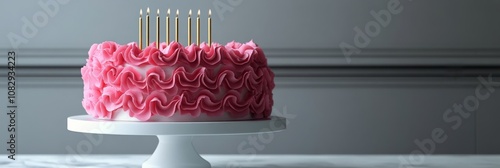 Elegant pink ruffled cake with candles displayed on a cake stand in a cozy se...