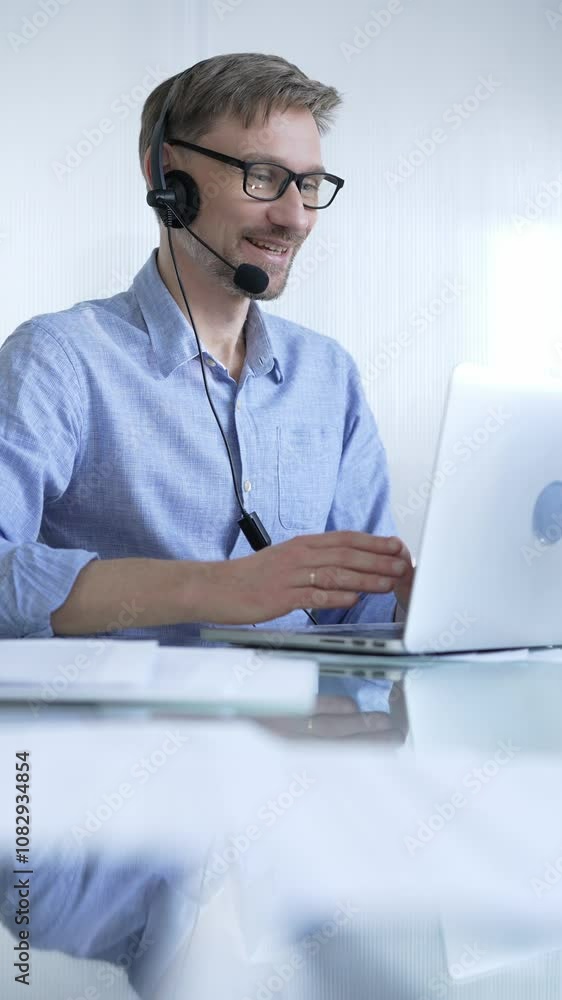 Male office worker demonstrates the significance of technology in modern business through client communication using laptop and headset. Business people concept