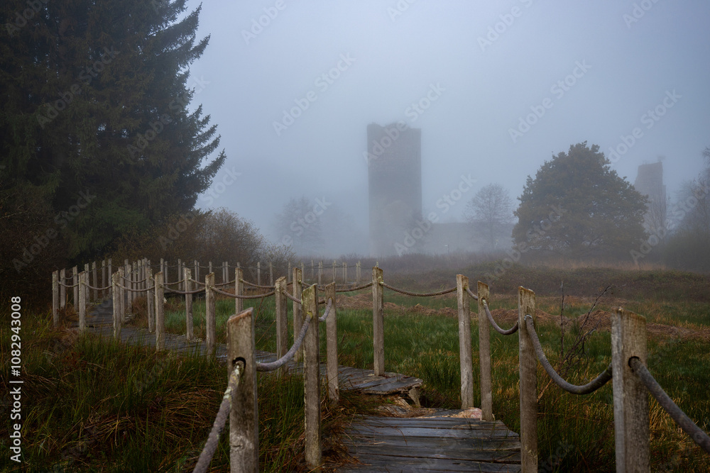 A wooden walkway or pier leads through a nature reserve in thick fog. Landscape shot in the middle of nature in autumn. Baldenau castle ruins, Morbach, Hunsrück, Rhineland Palatinate A wooden walkway or pier leads through a nature reserve in thick fog. Landscape shot in the middle of nature in autumn. Baldenau castle ruins, Morbach, Hunsrück, Rhineland Palatinate