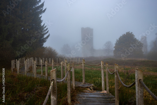 A wooden walkway or pier leads through a nature reserve in thick fog. Landscape shot in the middle of nature in autumn. Baldenau castle ruins, Morbach, Hunsrück, Rhineland Palatinate photo