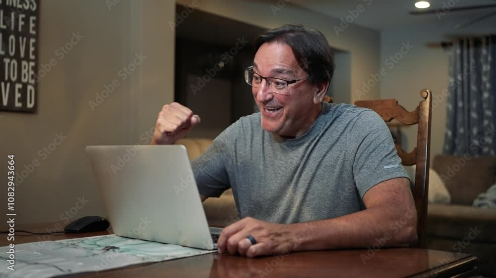 A man working at home uses his laptop to get good news, perhaps in an email. A man working at home uses his laptop to get good news, perhaps in an email.