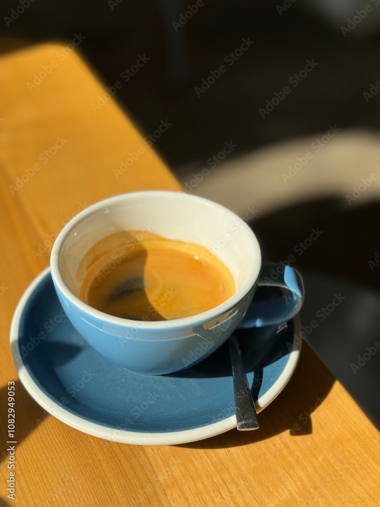 Morning espresso in a blue cup with natural sunlight casting shadows on a wooden table