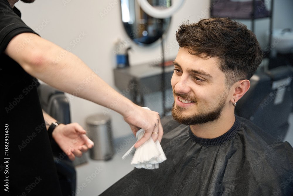 Haircutter brushes white powder onto happy client face Haircutter brushes white powder onto happy client face