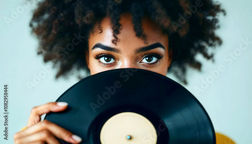 Portrait of beautiful black young girl with afro hair hiding behind vinyl record, shy woman, people lifestyle background