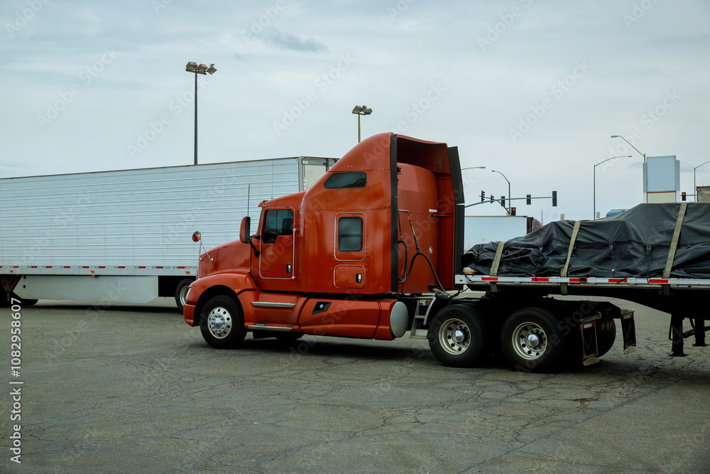 Semi truck with high cab is parked beside white trailer in busy parking lot. Semi truck with high cab is parked beside white trailer in busy parking lot.