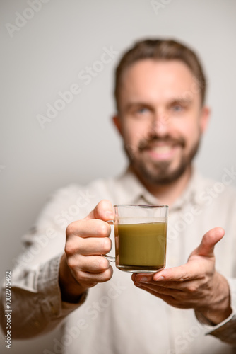 Kratom consumption concept: male bearded hipster holds a ready to drink glass of green liquid, powdered kratom melted in hot water, kratom tea, close up photo, selective focus