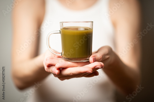 Kratom consumption concept:  female holds a ready to drink glass of green liquid, powdered kratom melted in hot water, kratom tea, close up photo, selective focus