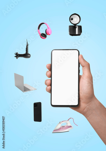 Internet shopping. Man holding mobile phone with blank screen surrounded by different home appliances and devices on light blue background