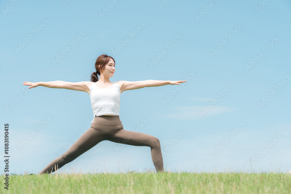 Fototapeta premium 青空の下でヨガ・ピラティス・ストレッチをする若いアジア人女性 