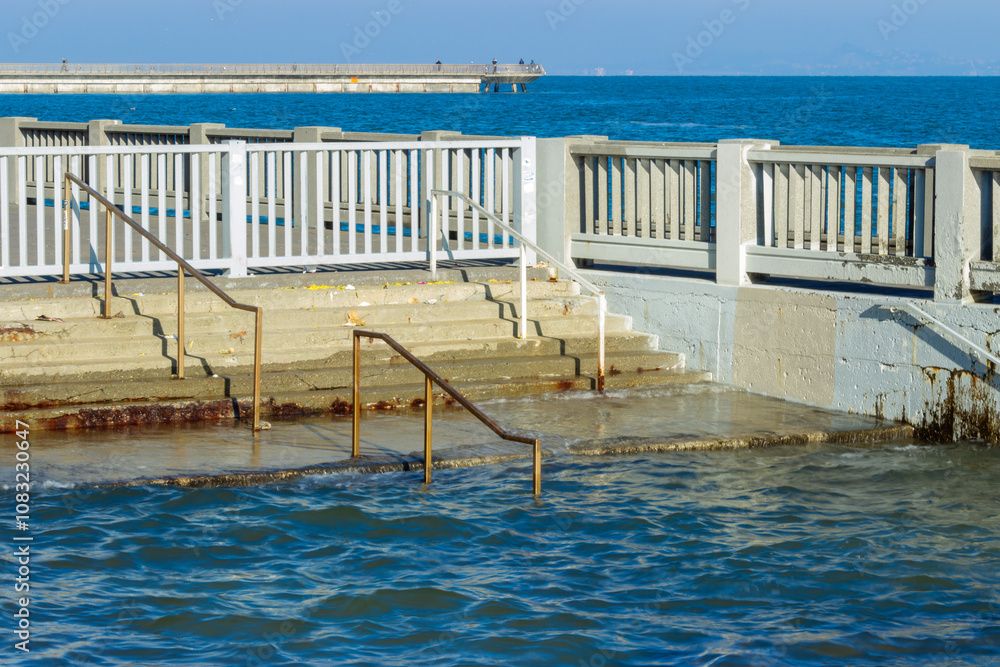 Steps and a railing near the Embarcadero in San Francisco submerged in water during a king tide, this scene highlights the impact of rising sea levels and coastal flooding on urban infrastructure.